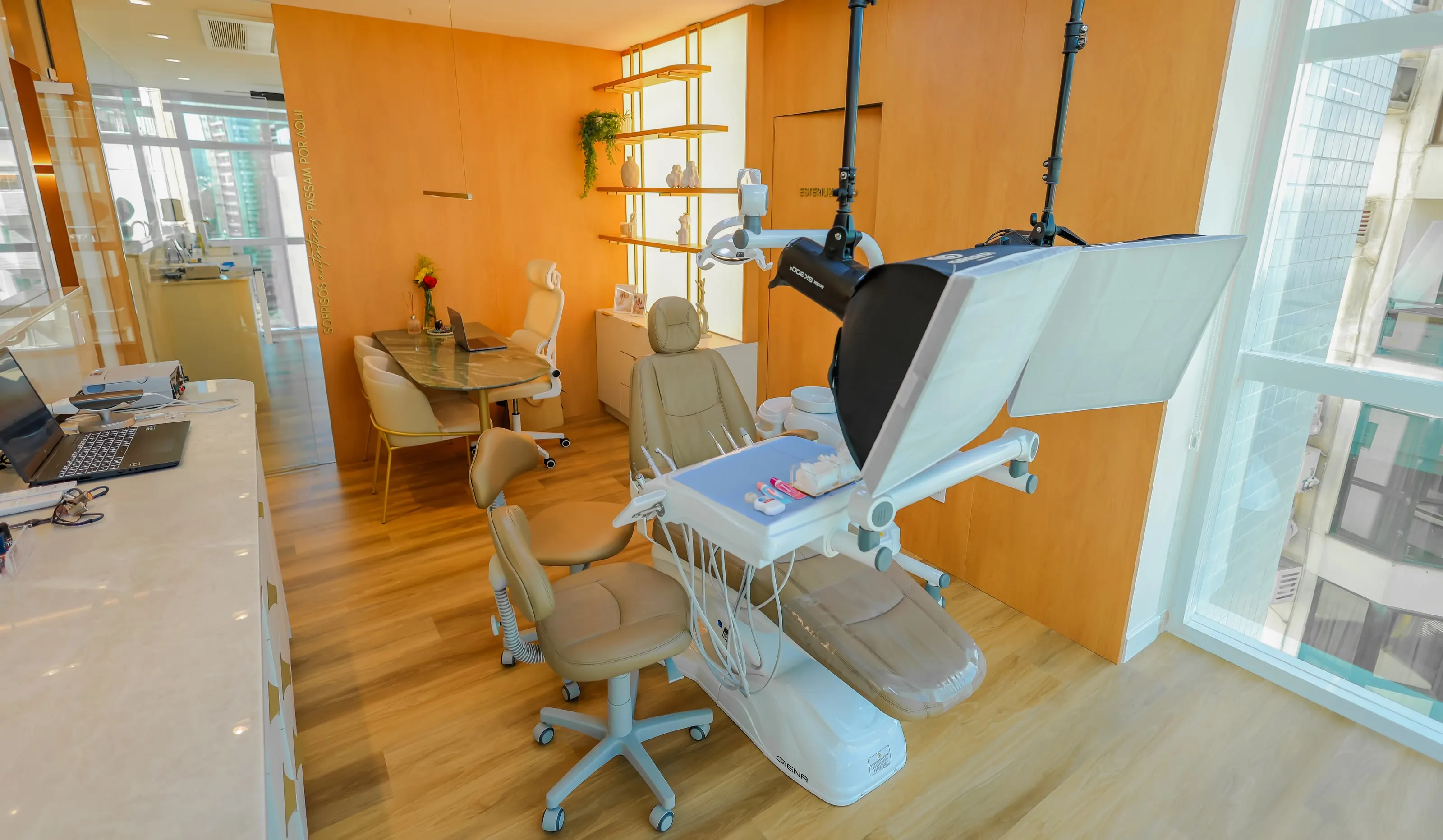 Sala de procedimentos do consultório, com a cadeira, os equipamentos e a janela para a cidade.