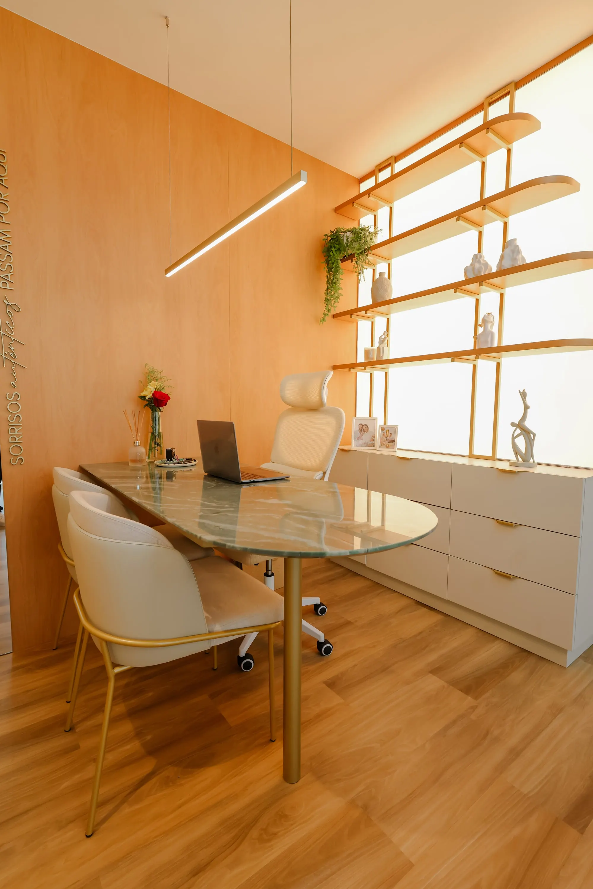 Mesa de atendimento do consultório, com as cadeiras e a estante iluminada ao fundo.