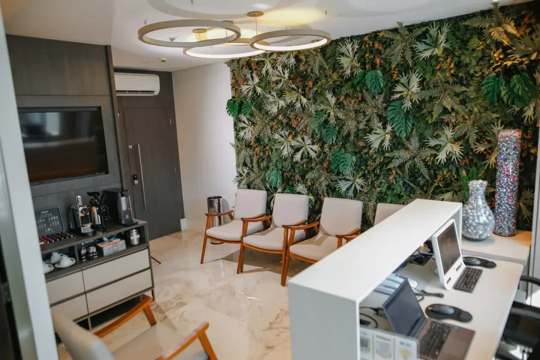 Entrada do consultório, com estação de café de um lado e poltronas diante de uma parede de plantas